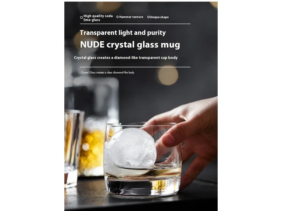 A hand holding a crystal whisky glass with a large ice sphere inside.