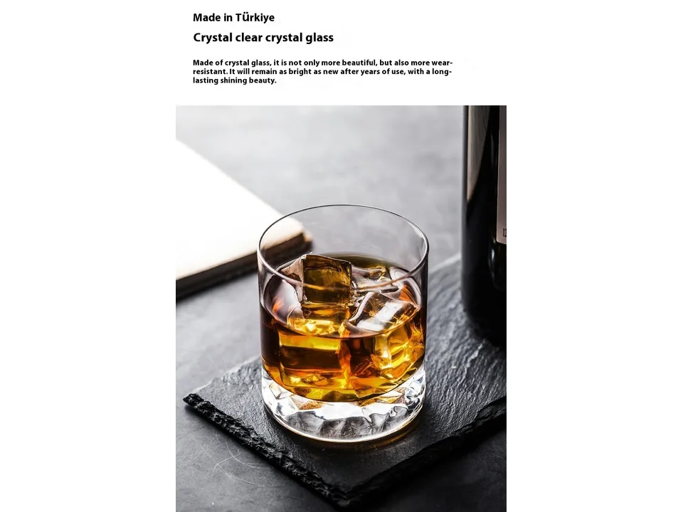 A crystal whisky glass filled with amber liquid and ice cubes on a slate coaster.