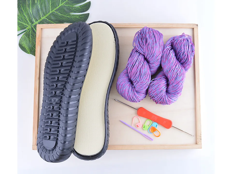 A DIY slipper kit containing a black sole, purple yarn, a crochet hook, and stitch markers.