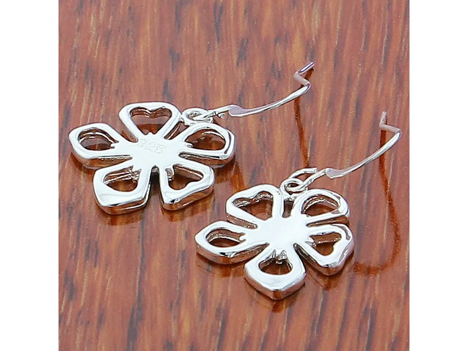 Close-up of silver flower-shaped drop earrings on a wooden surface.