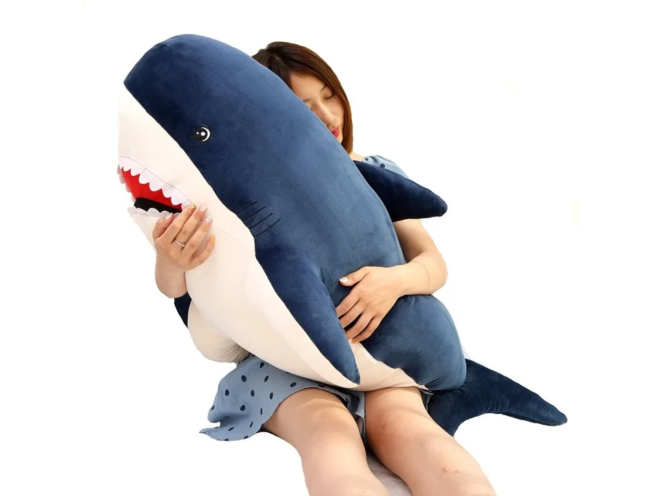 A woman hugging a large blue shark plush toy.