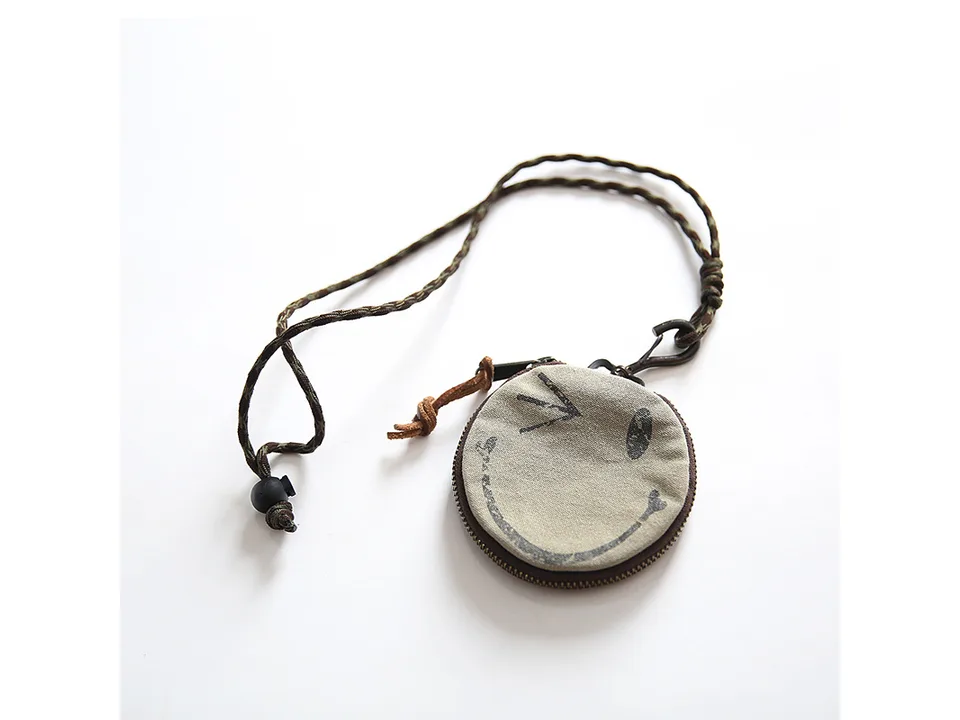 Round coin purse with a smiley face design and a long lanyard.