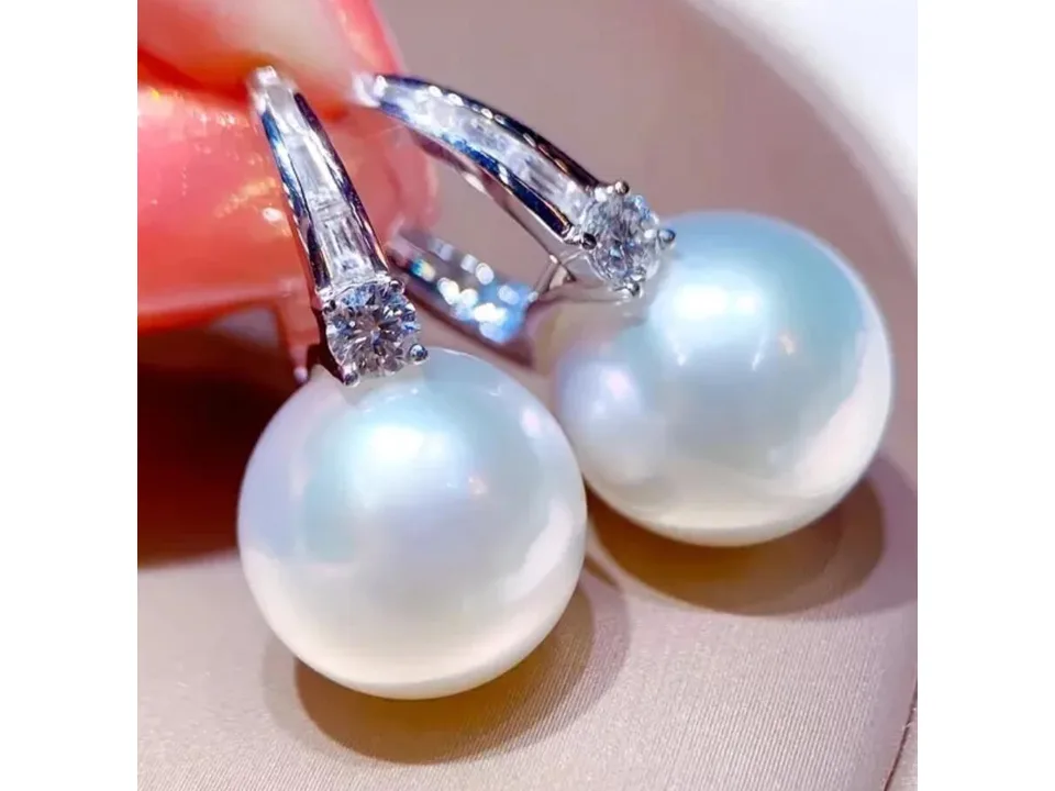 Close-up of elegant pearl earrings with zircon inlay held by fingers.