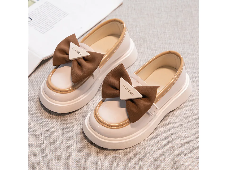 A pair of beige and brown girls' loafers with bows.