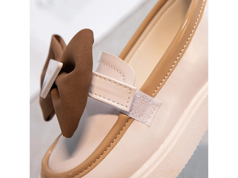 Close-up of the beige and brown girls' loafer showing the bow and velcro strap detail.