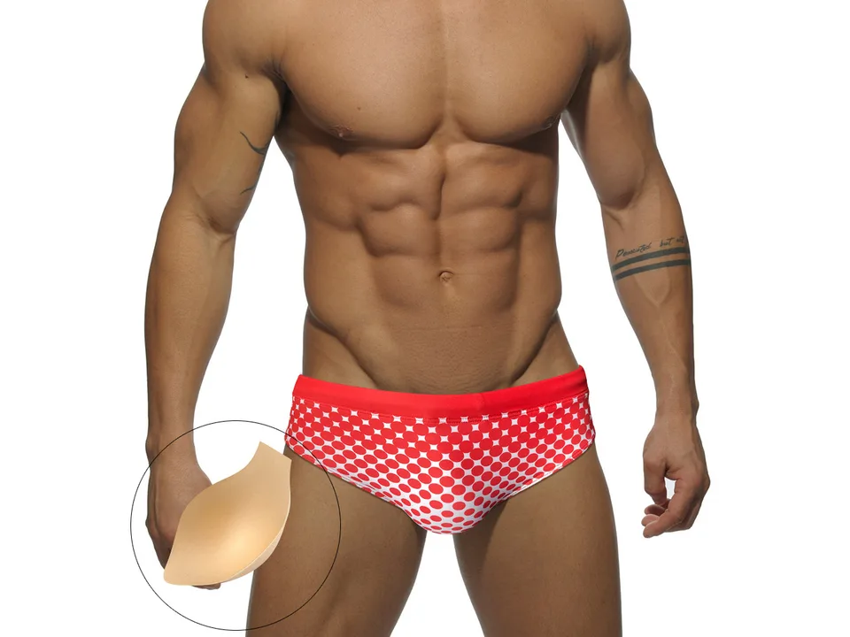 Model wearing red polka dot swim briefs with a removable padding insert shown in a circle.