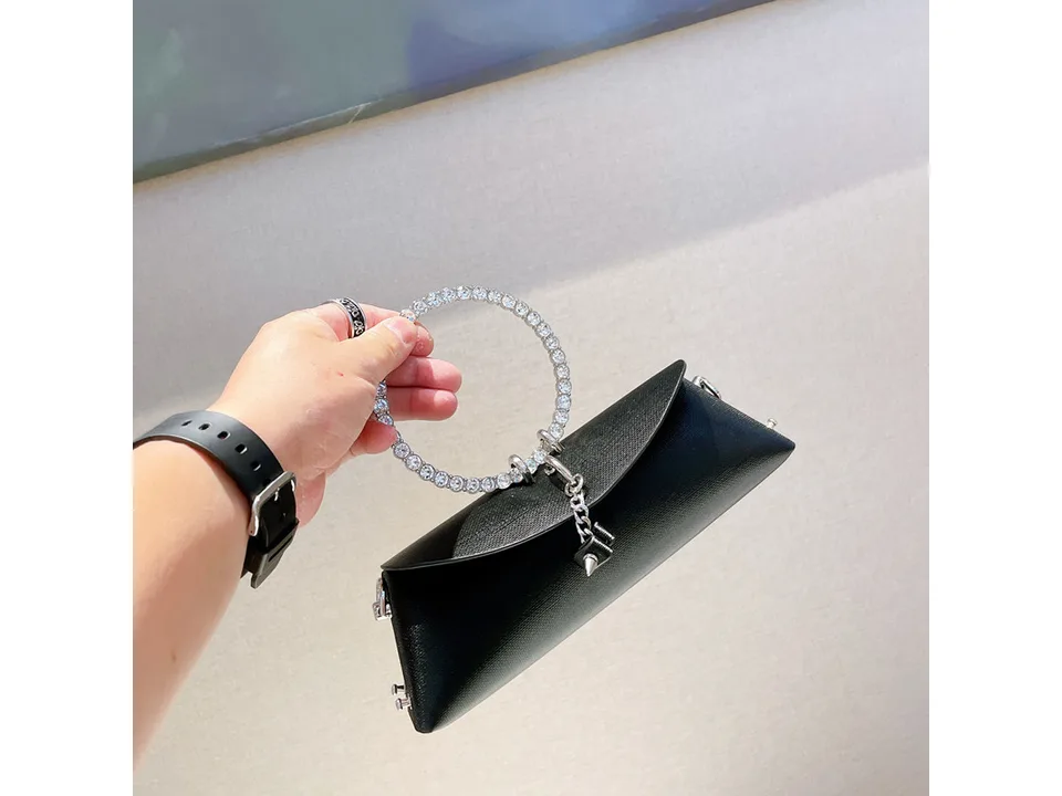 A small black handbag with a rhinestone ring handle and a decorative chain.