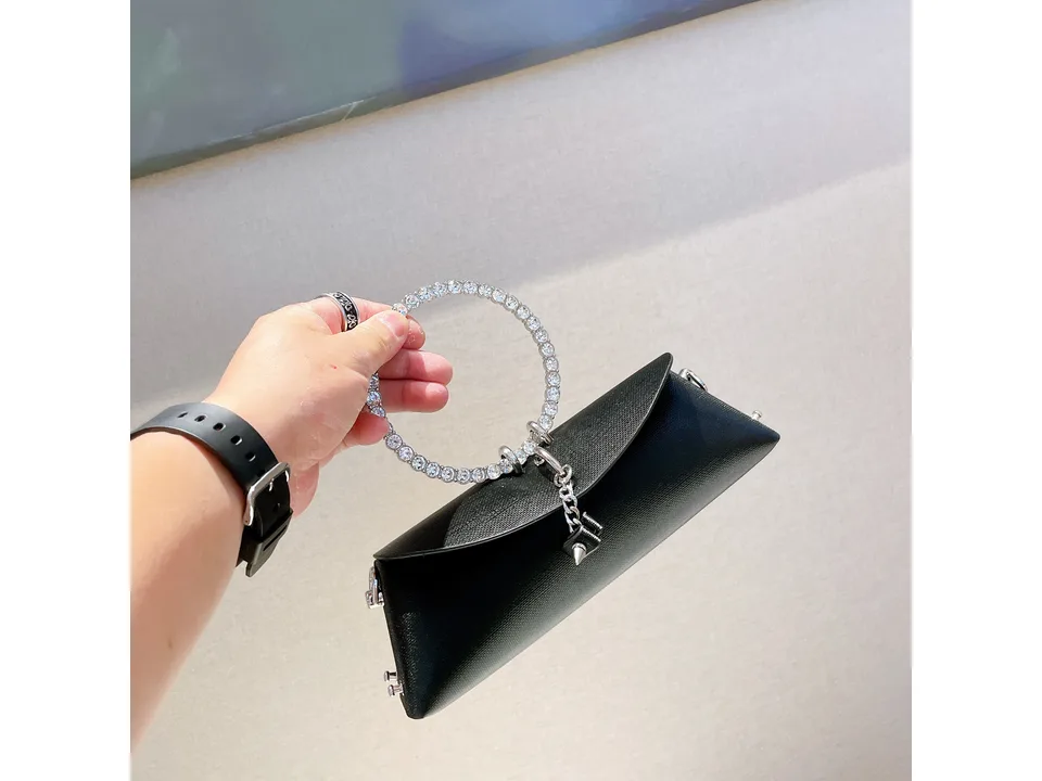 A hand holding a small black handbag with a rhinestone ring handle.