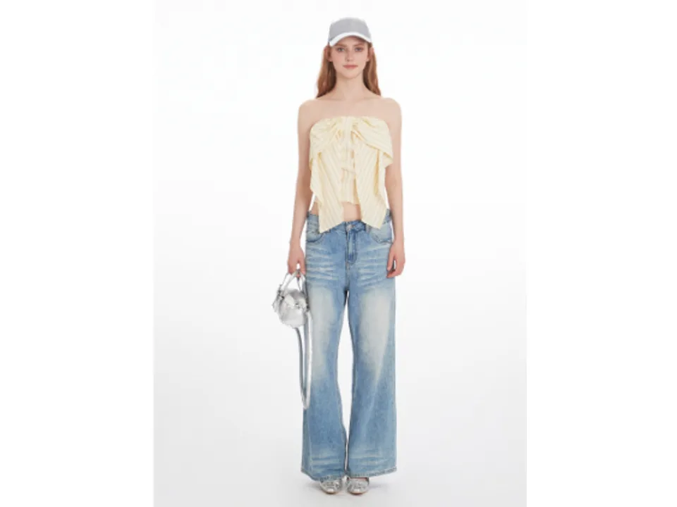 Full length view of a model wearing a striped strapless tube top with a bow detail and blue jeans.