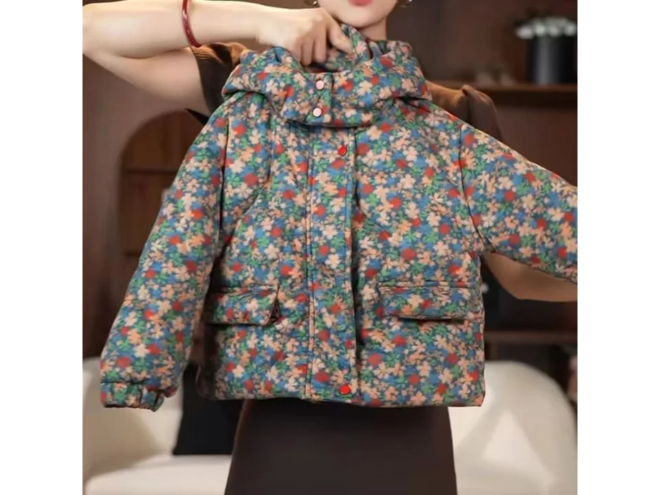 A person holding up the floral print winter coat to show the front.