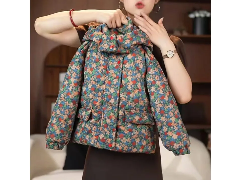 A person holding up the floral print winter coat to show the front.