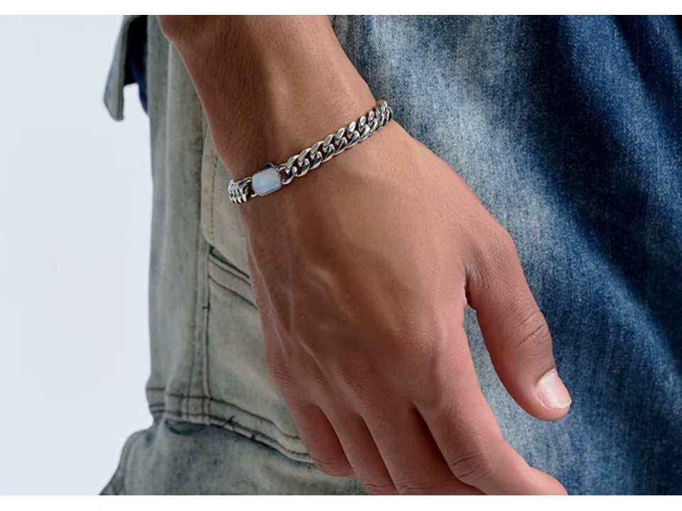 A silver Cuban link chain bracelet with a shell accent worn on a person's wrist.