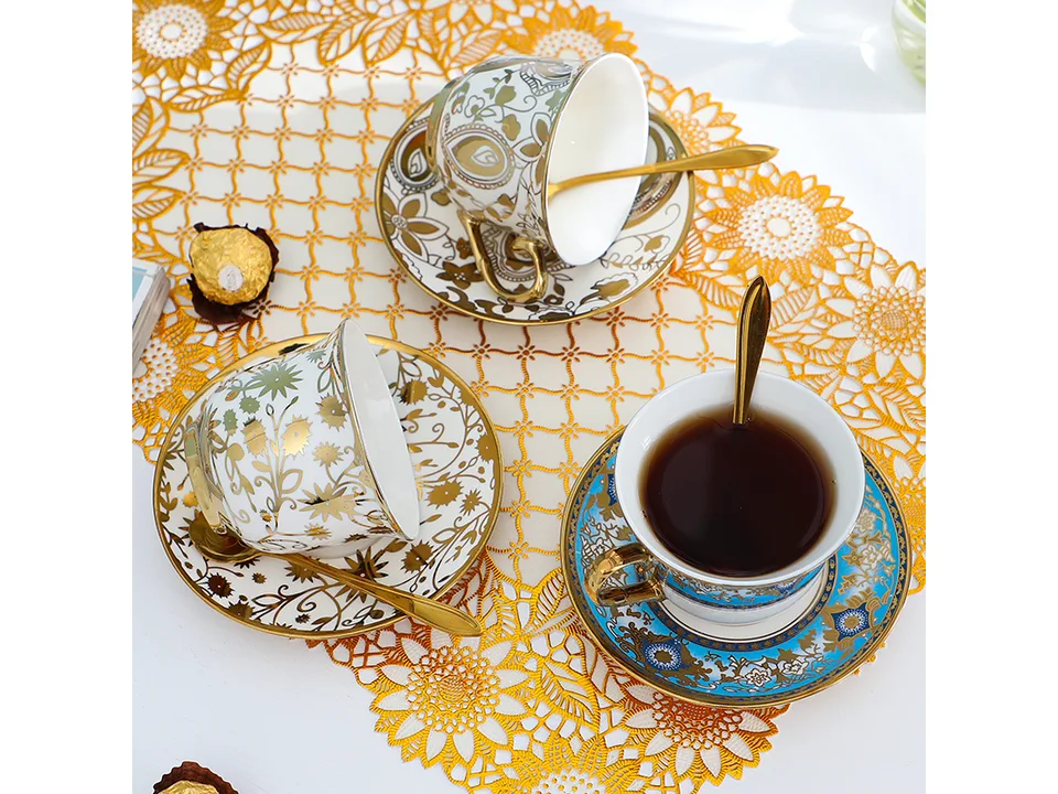 Three porcelain coffee cups and saucers with gold spoons arranged on a decorative lace tablecloth.
