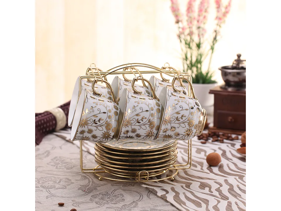 A set of gold-patterned white porcelain coffee cups and saucers on a gold metal rack.