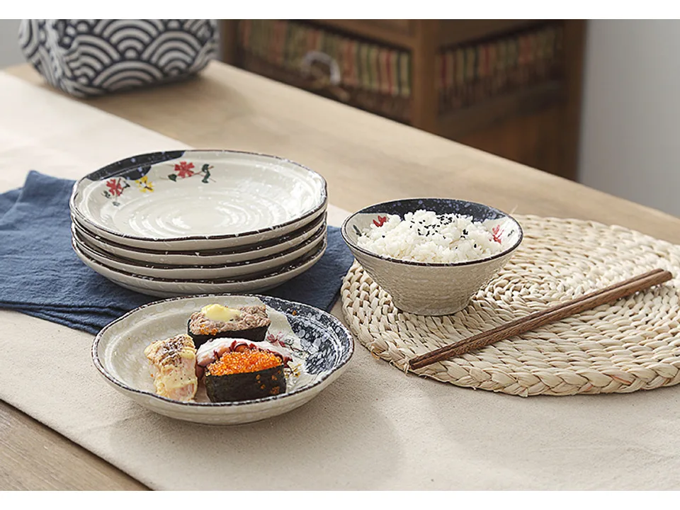 A stack of ceramic plates with a bowl of rice and sushi on a table.
