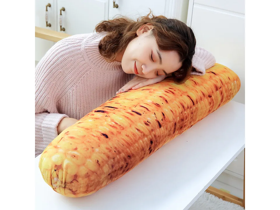 A woman resting her head on a large roasted corn plush pillow.