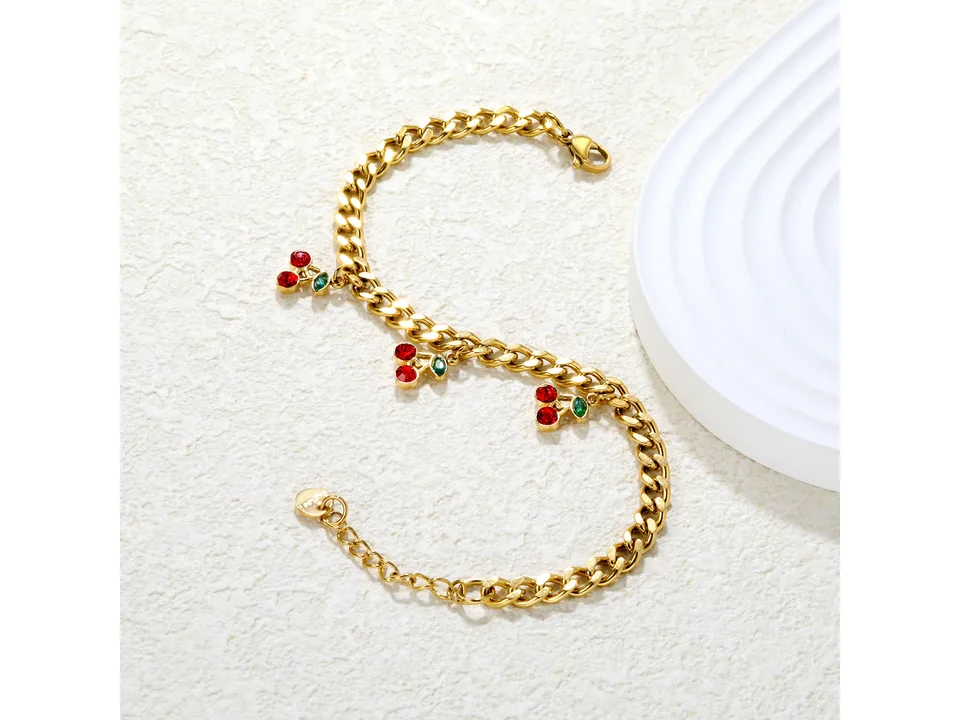 Gold-plated cherry charm bracelet arranged in an S-shape on a white surface.