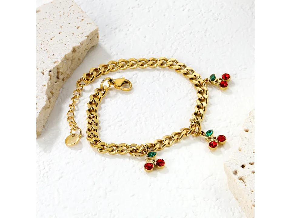 Gold-plated cherry charm bracelet displayed on a white textured surface.