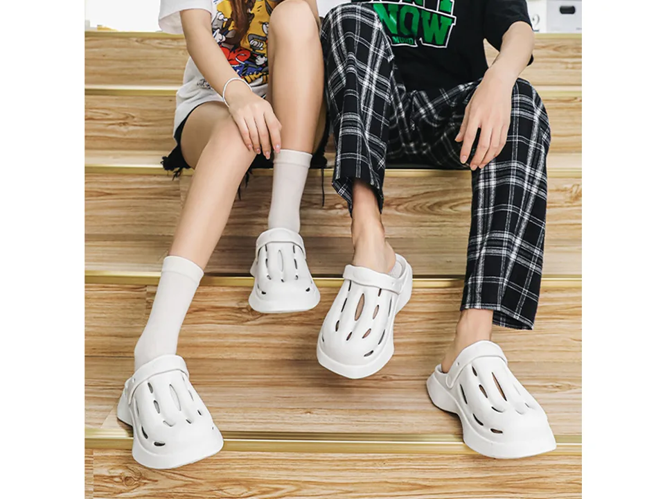 Two people wearing white casual EVA clogs while sitting on wooden stairs.