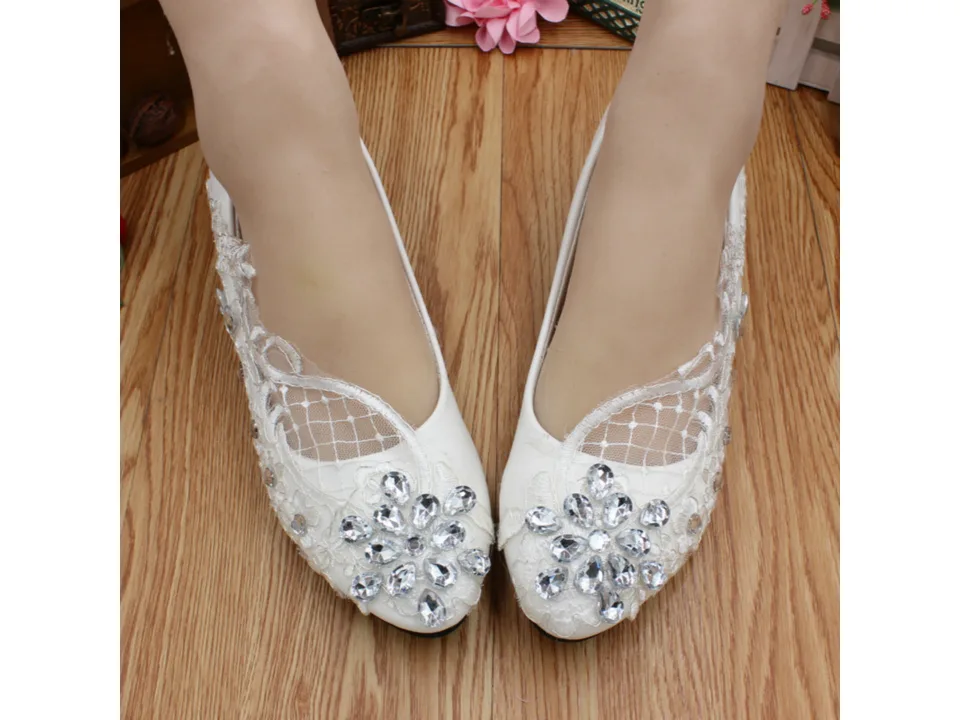 A pair of white low-heel shoes with lace and rhinestone floral details worn on feet.