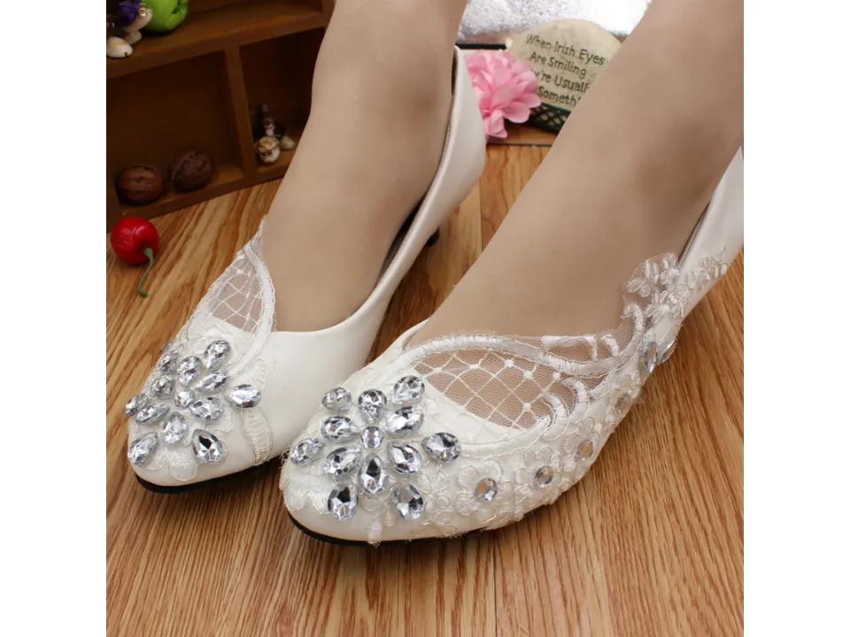 Close-up of white bridal shoes with rhinestone floral embellishments on a wooden floor.