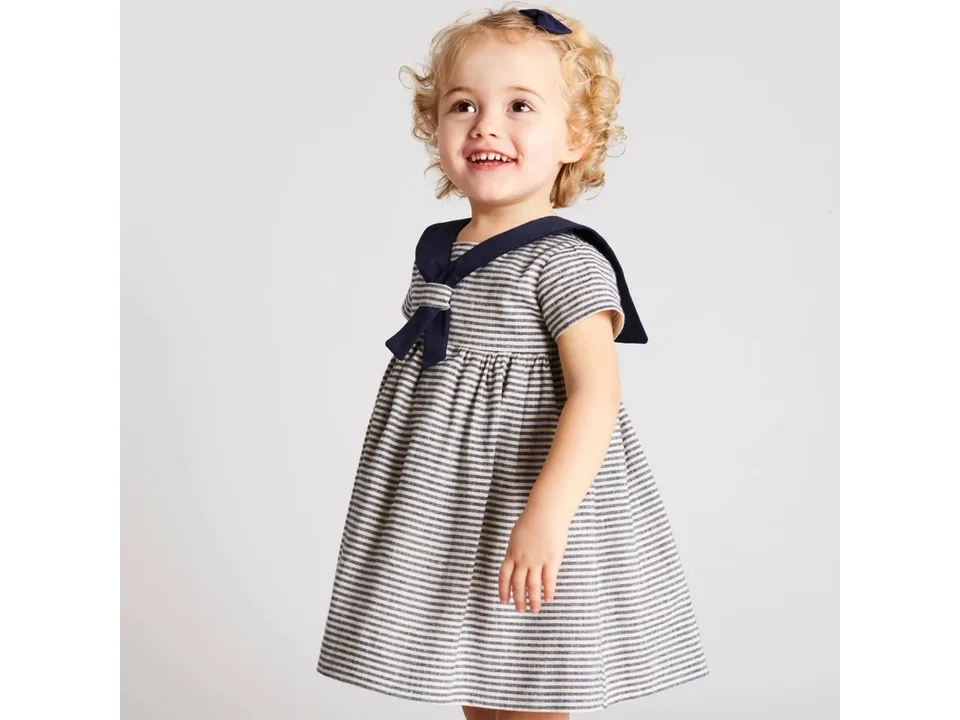 A young girl wearing a navy style sailor collar short-sleeve dress with striped pattern.