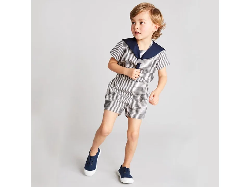 A young boy wearing a navy style sailor collar short-sleeve outfit with striped pattern.