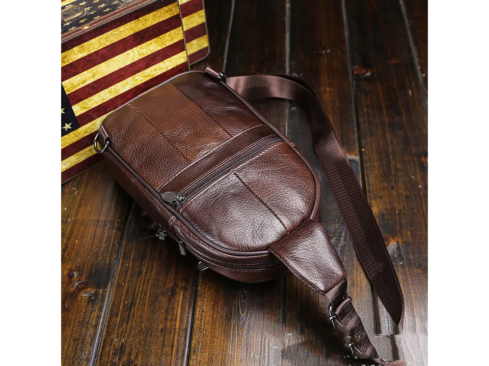 Angled view of the brown leather sling bag resting on a wooden surface.