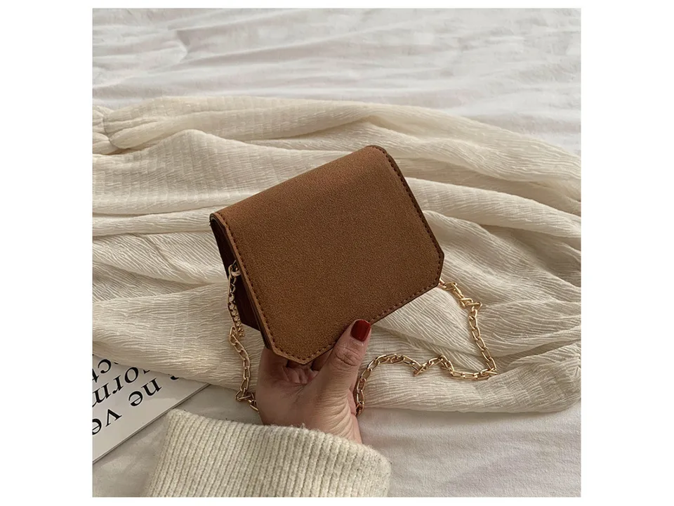 A small brown suede-like shoulder bag with a gold chain strap held in a hand.