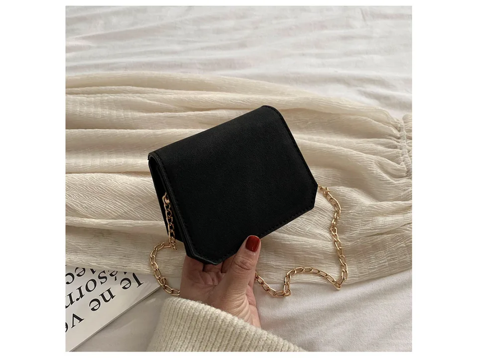 A small black suede-like shoulder bag with a gold chain strap held in a hand.