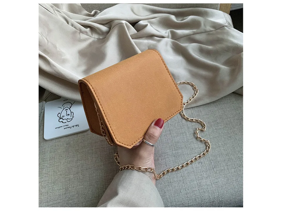 A small tan suede-like shoulder bag with a gold chain strap held in a hand.