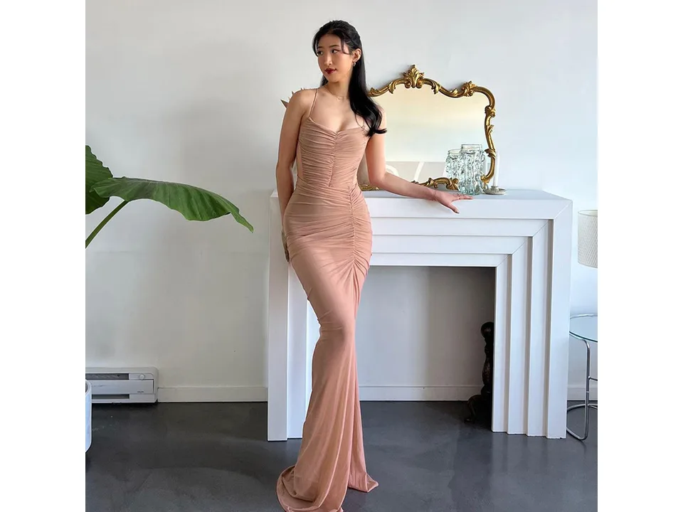 A woman posing in a sleeveless, ruched, bodycon maxi dress.