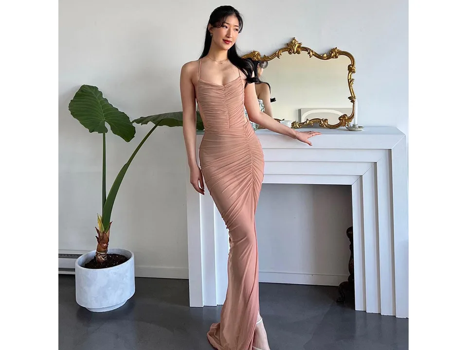 A woman wearing a sleeveless, ruched, bodycon maxi dress in a studio setting.