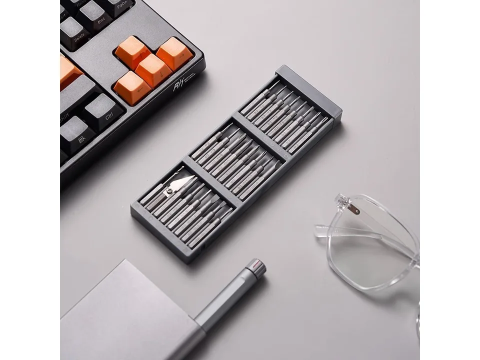 Precision screwdriver set in an open grey case next to a keyboard and glasses.