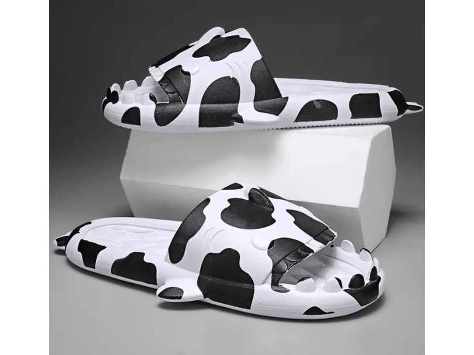 A pair of white and black cow-print shark-themed slides.