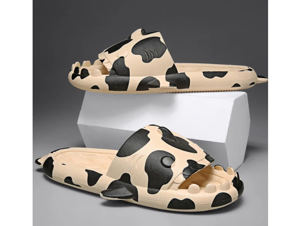 A pair of beige and black cow-print shark-themed slides.