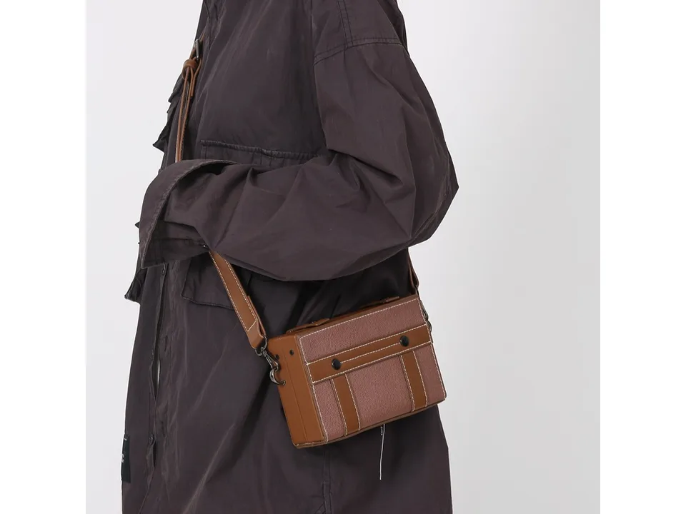 A person wearing a brown box-style crossbody bag.