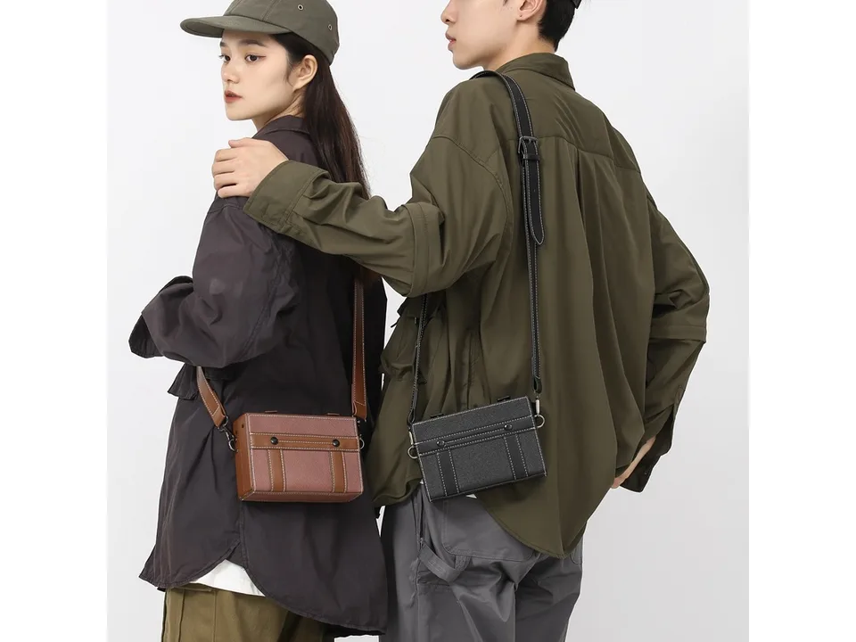 Two people standing side-by-side, one wearing a brown crossbody bag and the other a black one.