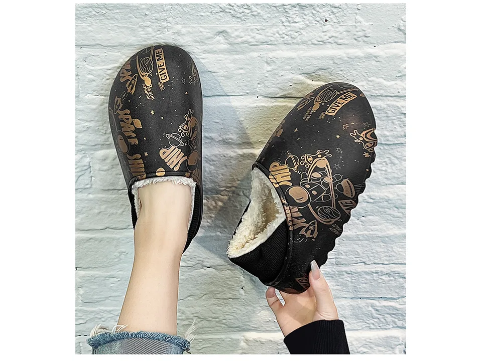 Person holding black space-themed plush-lined mules.