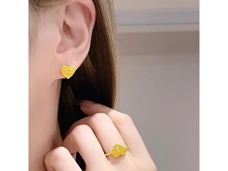 A person wearing a gold heart stud earring and a matching heart ring.