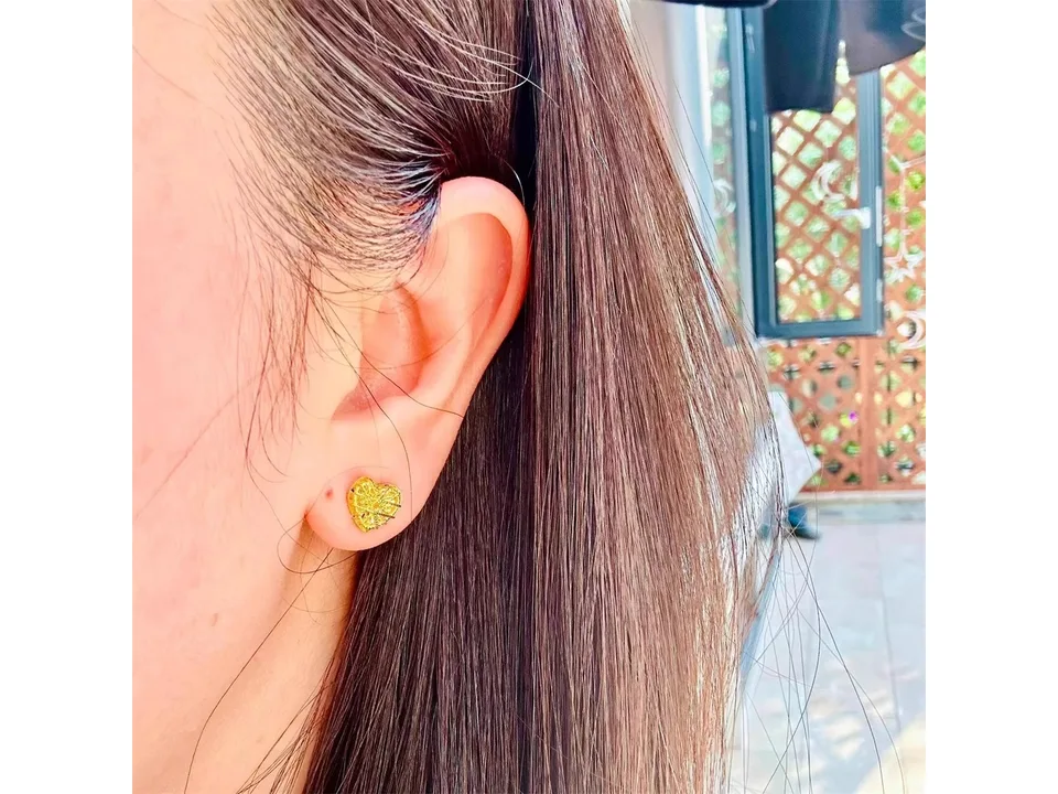 Close-up of a gold textured heart stud earring worn on an earlobe.