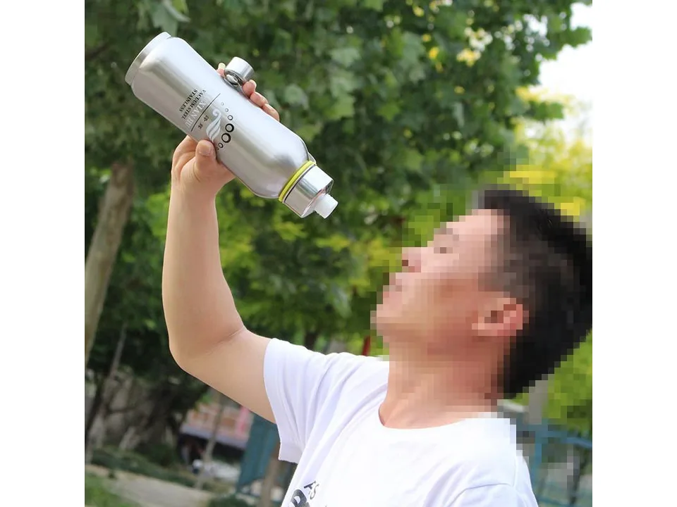 A person drinking from a stainless steel vacuum insulated water bottle outdoors.