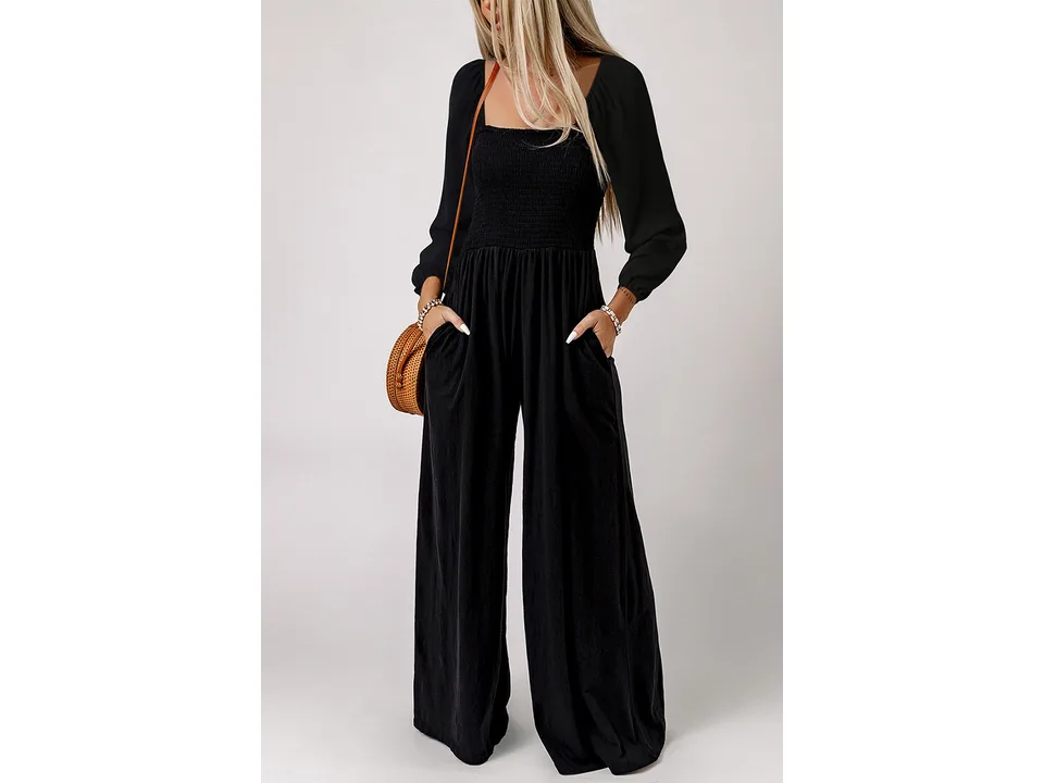 A woman wearing a black long-sleeve wide-leg jumpsuit with a smocked bodice and pockets.