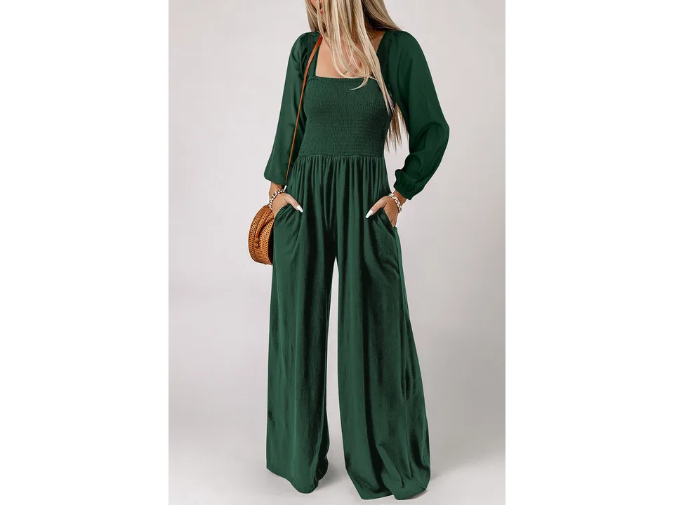 A woman wearing a dark green long-sleeve wide-leg jumpsuit with a smocked bodice and pockets.