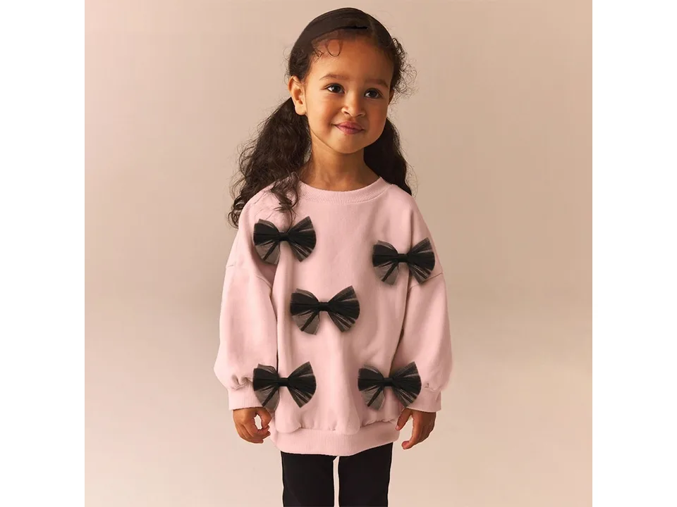 A young girl wearing the pink sweatshirt with black bow accents.