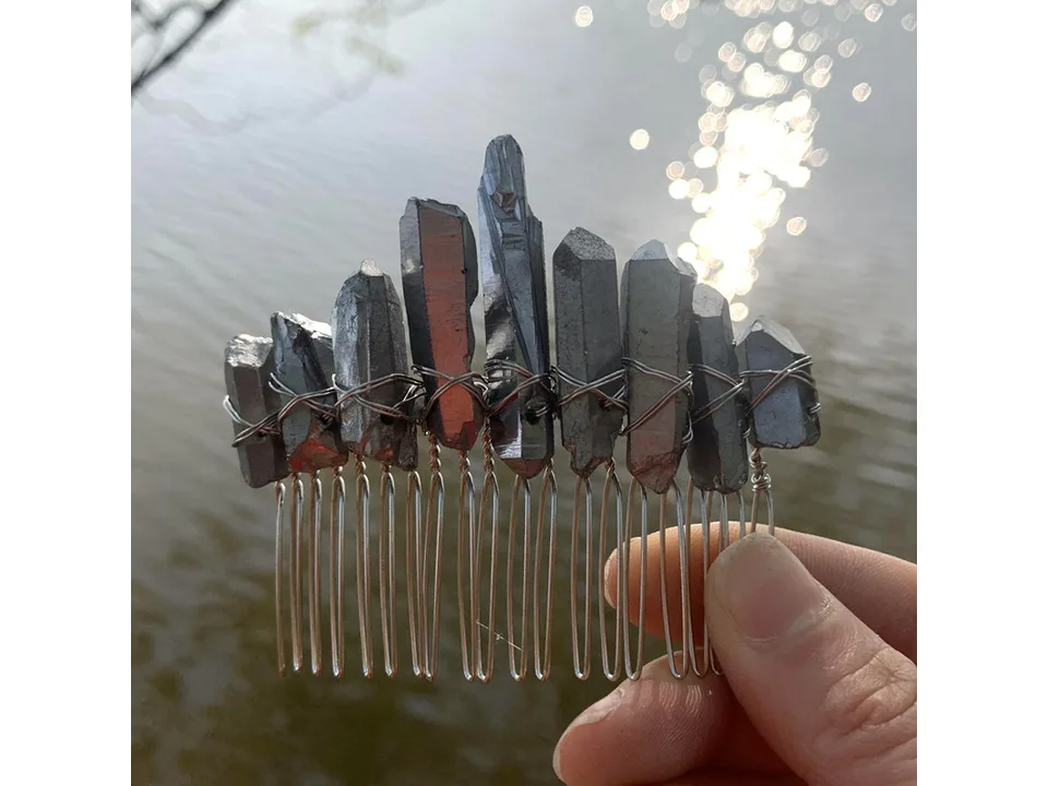 A hand holding a grey crystal hair comb against a water background.