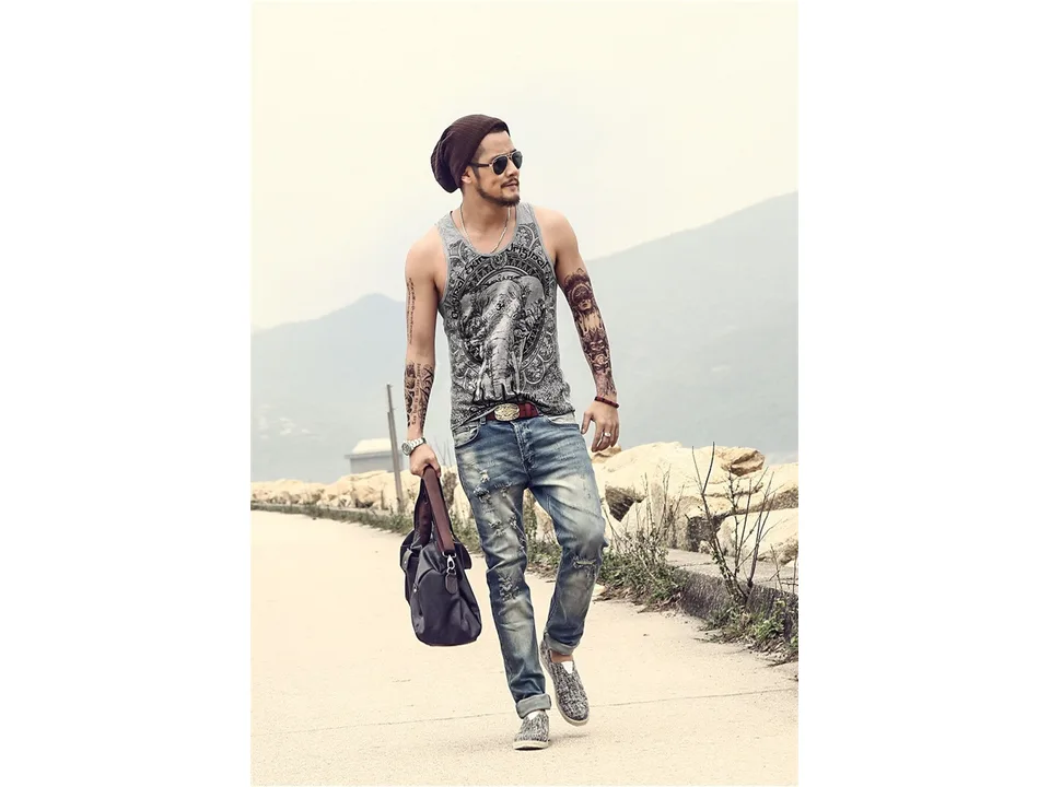 A man wearing a grey tank top with an elephant print design, walking and carrying a bag.