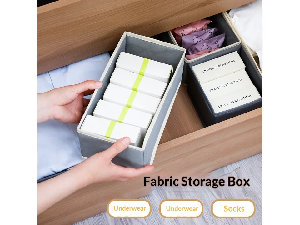 A person placing a grey fabric storage box filled with small white boxes into a wooden drawer.