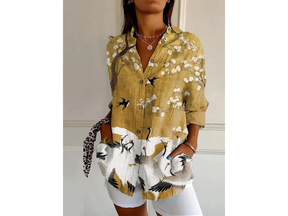 A woman wearing a long-sleeve button-down shirt with a yellow and white crane bird print.
