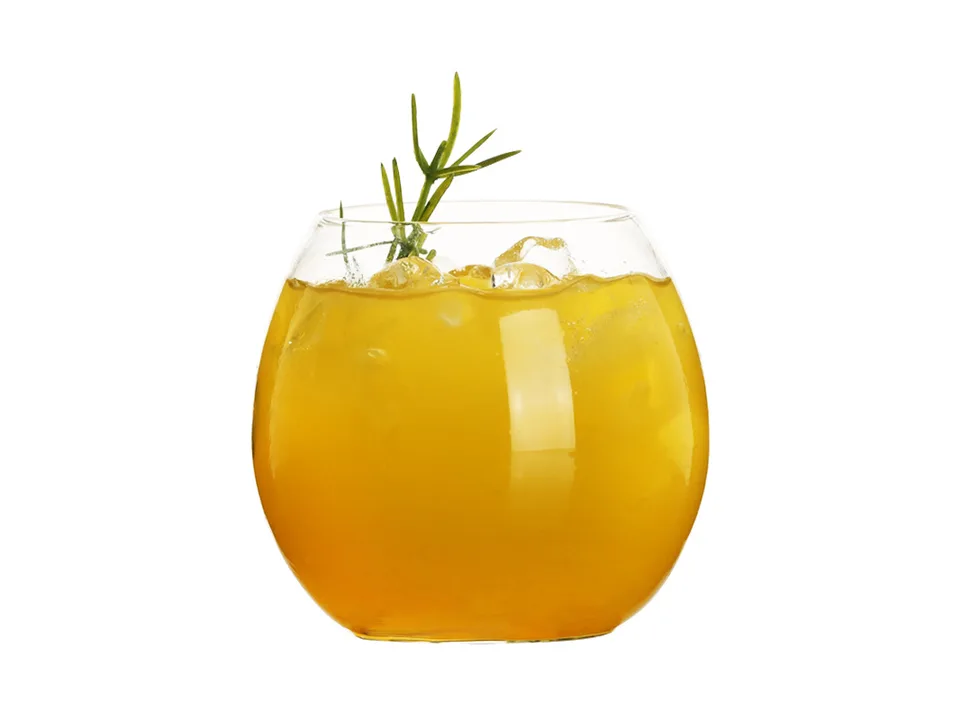 A round pot-belly glass cup filled with an orange drink and ice, garnished with a sprig of rosemary.